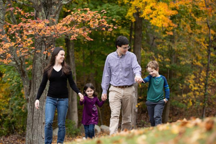 A photo of a family of four walking at the edge of the woods