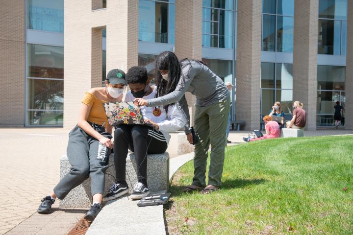 A photo of a group of students outside looking at a computer