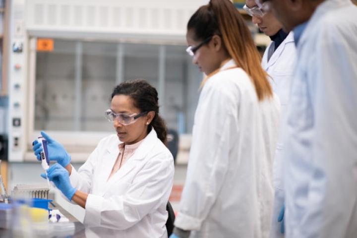 A photo of a young women using bio lab materials with other students looking on