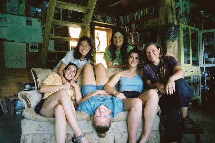 Six people pose in various positions on and behind a couch. 