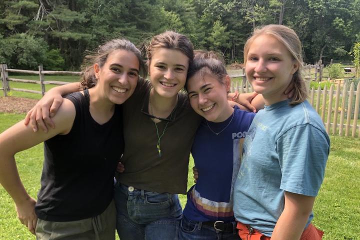 Four smiling students pose shoulder-to-shoulder in the summertime sunshine.