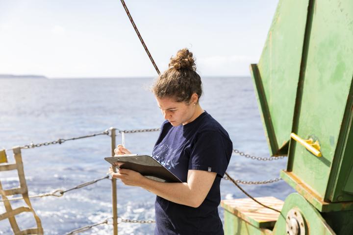 Riva Gulassa ’15 holds a clipboard while working at sea.