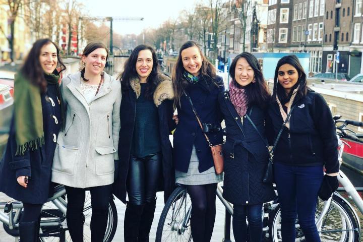 (L to R): 2013-ers Rachel Bobbins, Jessica Bethune, Andrea Cuadra, Teddie Vidolova, Alison Shin, and Aiswarya Kolisetty reunited in Amsterdam in 2019. Six friends pose on the street during a reunion in Amsterdam in 2019.
