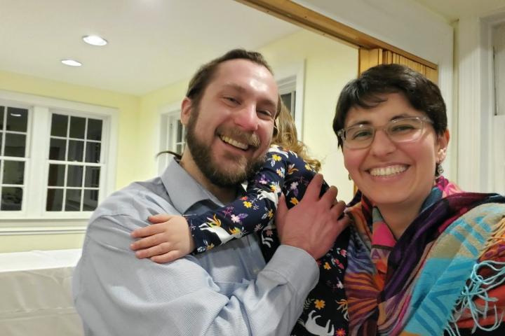 David '07 with Aurelia and Juliana '07 at a friend's wedding, April 2022 Two people pose and smile for a photo, with the person on the left holding a small child whose face is obscured as they are snuggling in close.