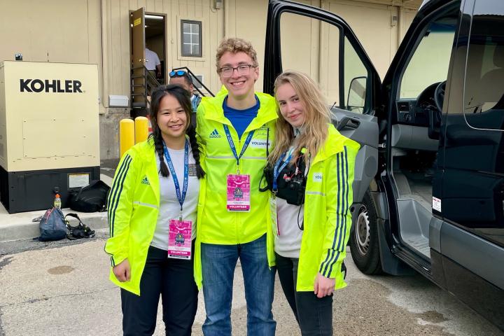 Three people in neon yellow windbreaker jackets pose for a photo in front of a van.