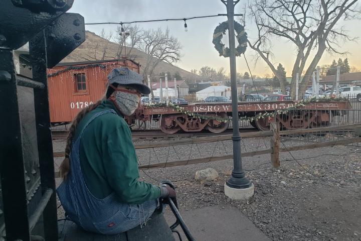 Jennifer Anderson '16 sits on a bench at Colorado Railroad Museum's Polar Express. A person in hat and face mask sits on a bench at Colorado Railroad Museum's Polar Express.