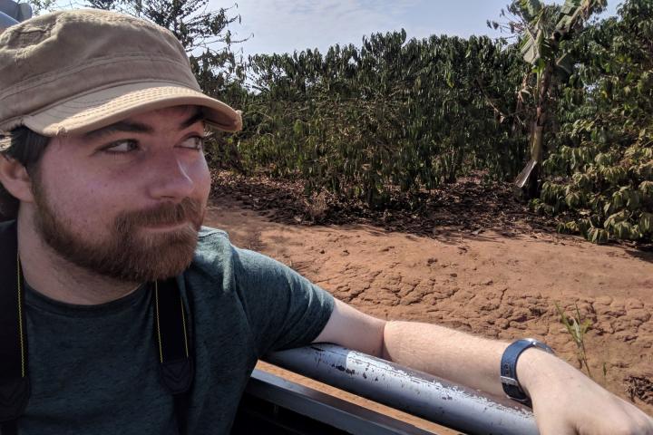 Mike Taylor '10. A man with a tan hat, brown beard and mustache, is sitting outside.