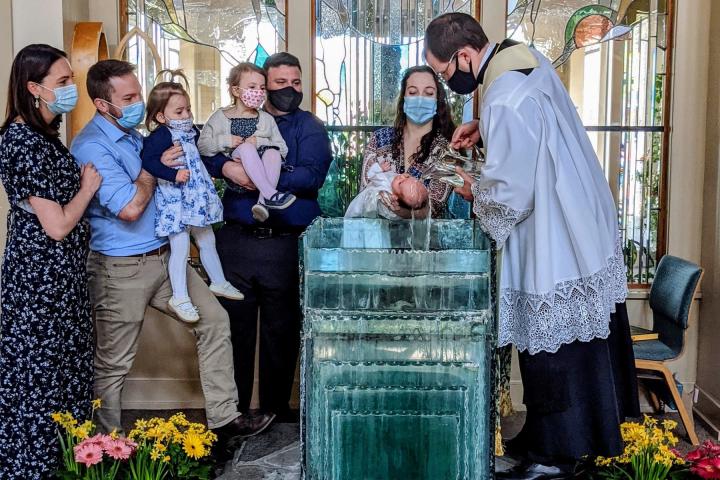 Multiple people attending a church baptism stand on the altar while a baby is baptized with water.