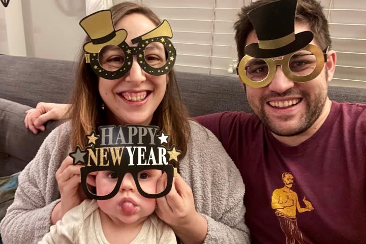 Brittany Strachota '13 with Michael Heyns '13 and their offspring, Arthur celebrating the beginning of 2022. A woman and a man and their child all wearing cardboard party glasses celebrating the New Year.