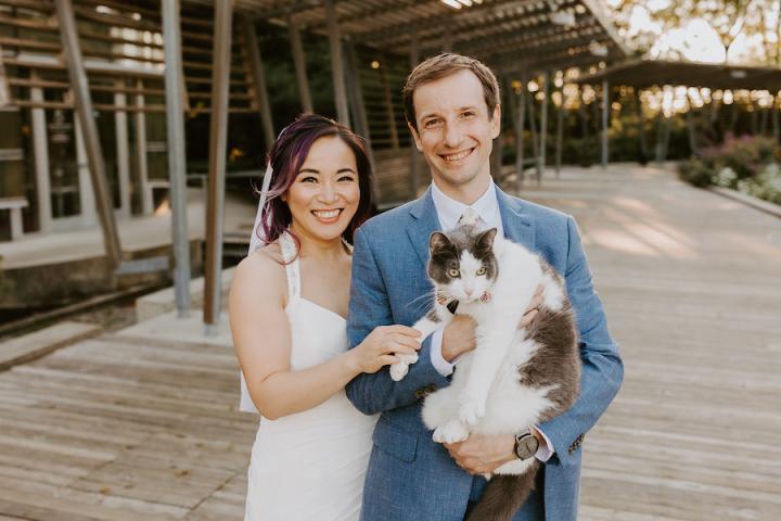 Liang Ding and Tim Smith '09 reprising their wedding photos with feline companion Molson in Queen Elizabeth Park, September 2021. A bride and groom pose for wedding photos with the groom holding a feline companion Molson in Queen Elizabeth Park, September 2021.
