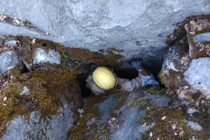 Adam Selker '20 dropping into a cave in California. Man with yellow helmet and dark blue gloves is squeezing down between a tight space in a cave.