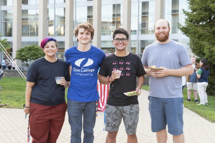 Four students stand facing the camera on the Olin College campus.