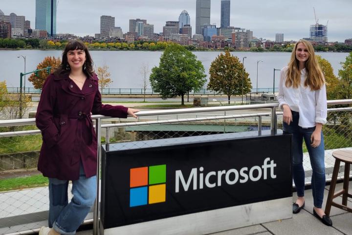 Two young women stand on opposite sides of an outside Microsoft sign.