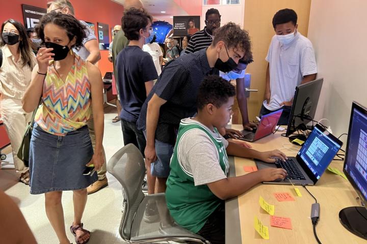 A college-aged student bends over to help a young student working on a laptop.