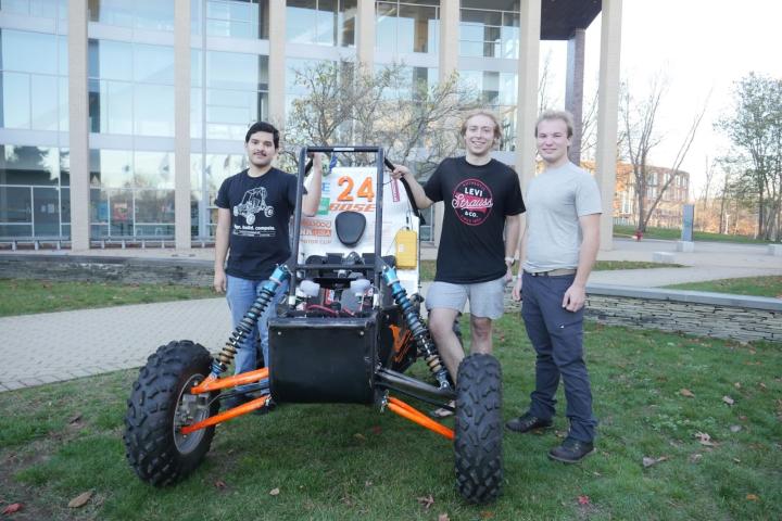 students standing next to an off-road vehicle