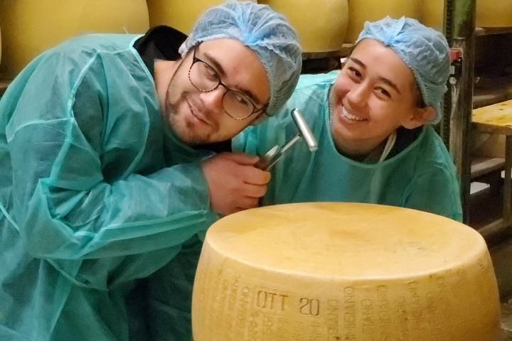 Two college students wear green protective smocks and hats as they tour a cheese factory in Italy