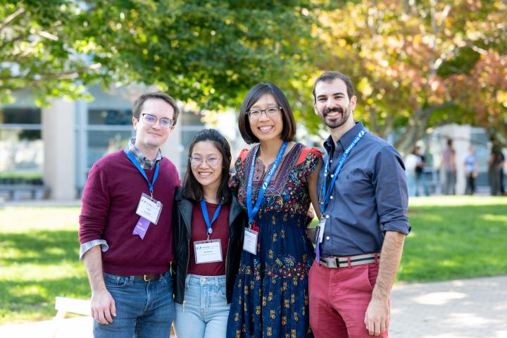 Four alum standing in the Olin O smiling at the camera