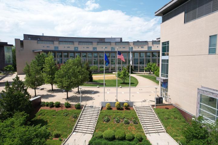 An overhead drone image of a college campus with buildings and three flags shown. 