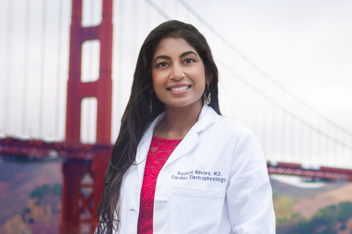 A woman wearing a white lab coat stands in front of the golden gate bridge