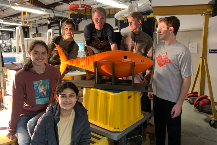 Six students pose for a group photo around a medium-sized, orange-colored ROBO-TUNA.