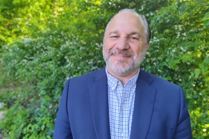 Sal Liberto, Interim Dean of Admission and Financial Aid A photo of a man in a blue jacket standing in front of a green bush
