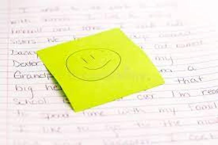 Piece of paper with text written on it and yellow sticky notes with a smiley face on top.
