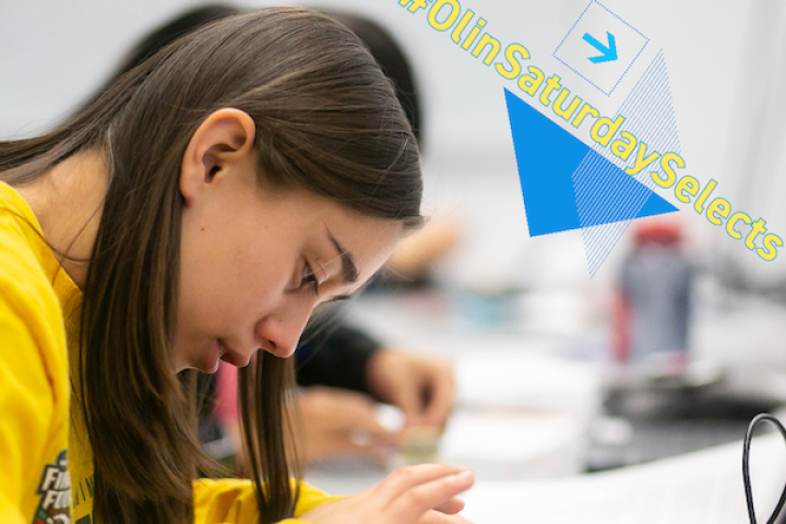 An Olin student wearing a bright mustard/yellow sweatshirt works with her hands on some multi-colored wires in a classroom.