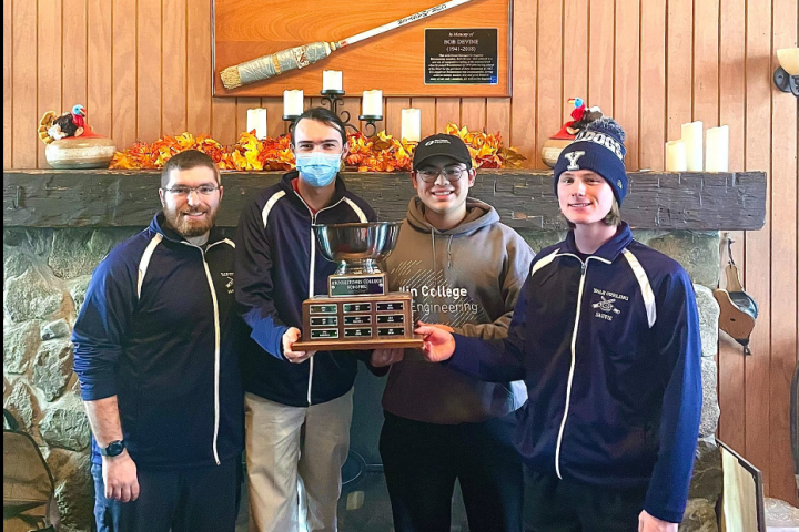 Olin College student Christopher Vidaurrazaga '27 - a curler with the Broomstones Curling Club, poses with his team and their trophy after winning a College Bonspiel.