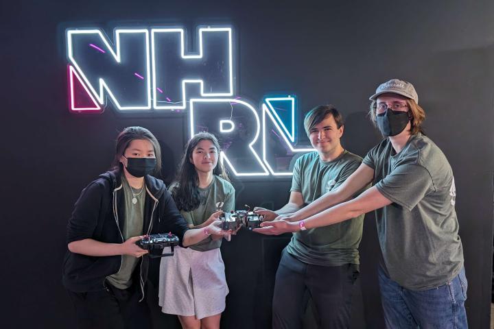 Four students hold a 3lb robot in front of a sign that reads "NHRL"