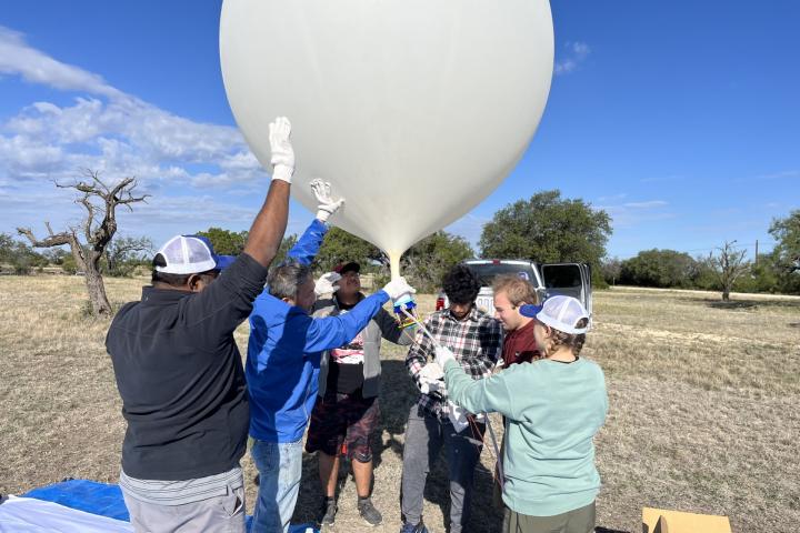A team of people hold up an inflated weather balloon with a blue sky in the background.