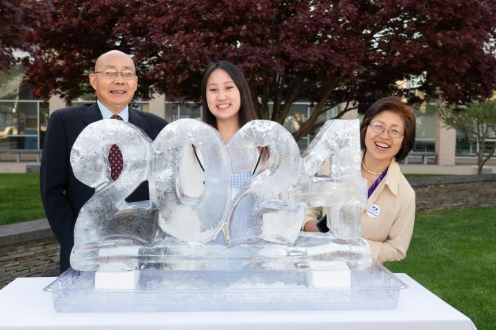 A family of three people take a photo behind an ice sculpture reading "2024."