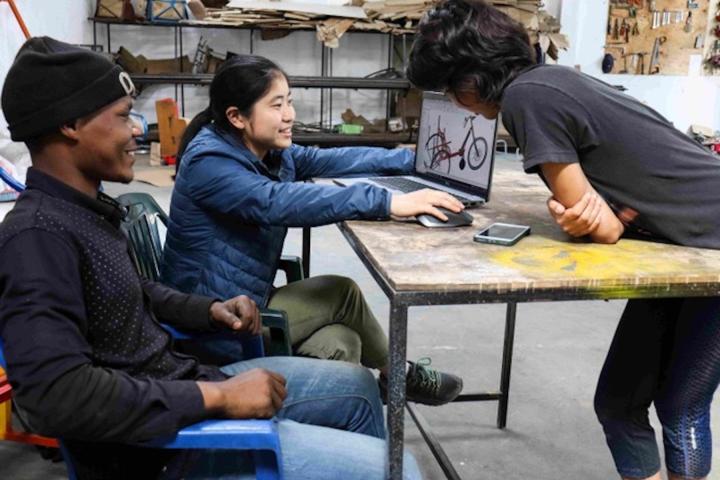 Three people shown looking at a laptop screen that displays a tricycle. 
