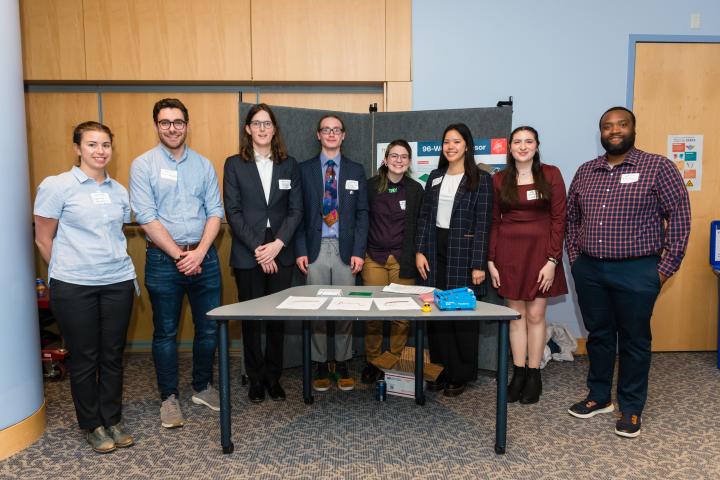 Students posing in front of project poster with liaison