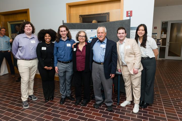 Students posing in front of project poster with sponsors
