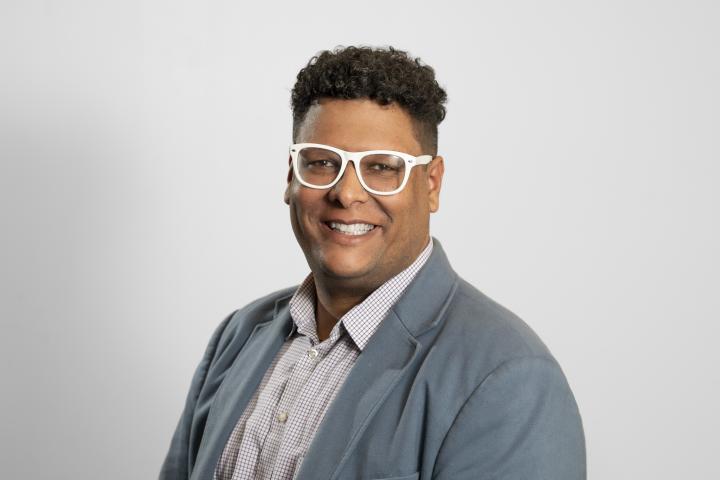 Jesse Austin-Breneman portrait, white glasses, curly hair, smiling at camera