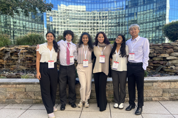 Five Olin College students and one faculty member are shown at the FIE 2024 conference standing in front of a window-filled building.