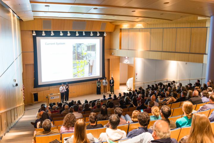 Students presenting slides in packed auditorium 