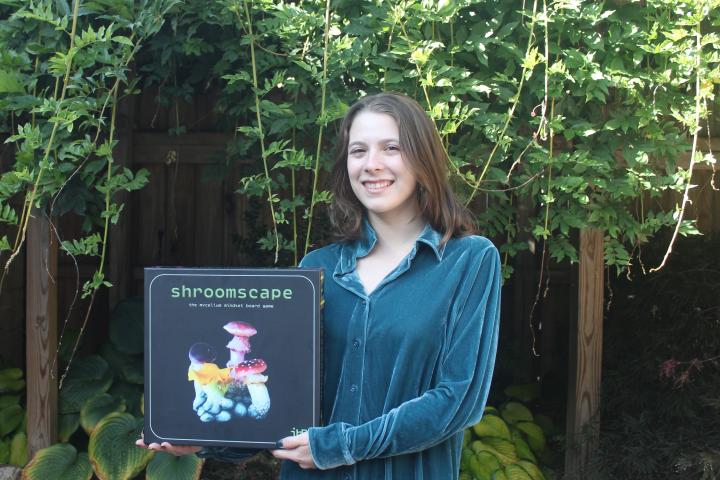 Camille Girard '21 holds their new game, Shroomscape: The Mycelium Mindset Board Game