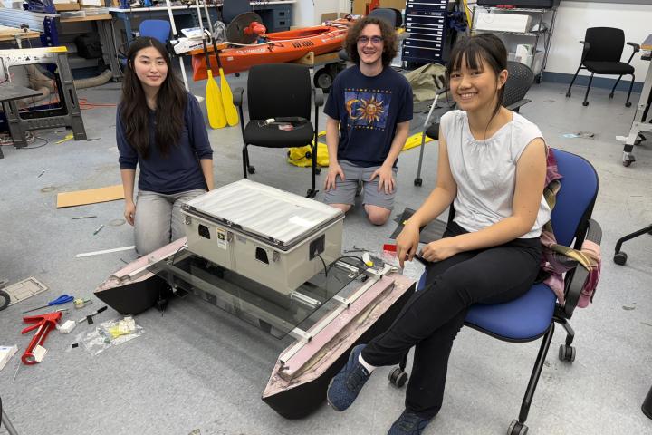 Three Olin engineering students pose with their small-scale autonomous surface vessel, made at Olin College as part of the CREST Lab.