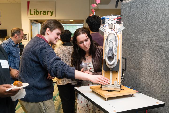 Student explaining their prototype in front of project poster at Summit