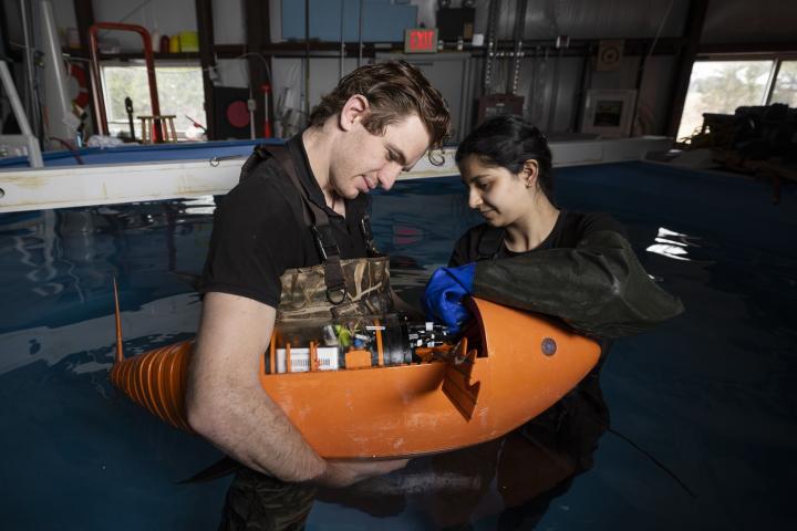 Engineering for people postcard showing two students holding a robofish in a tank of water.