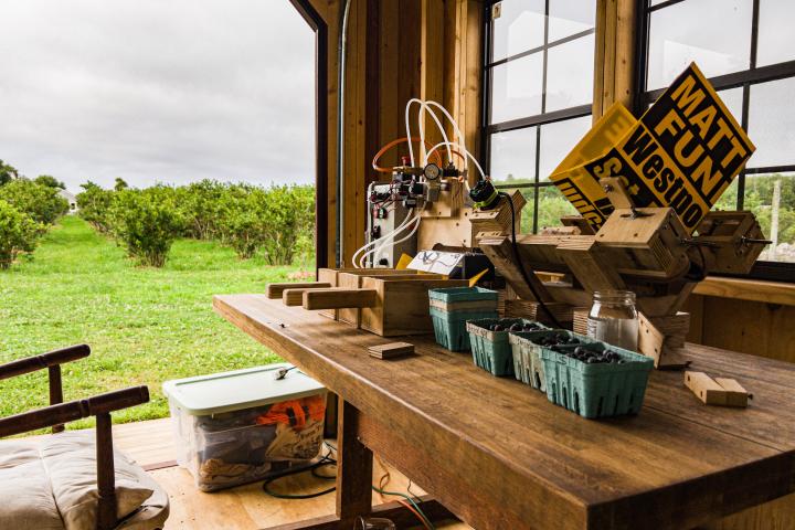 The Automated Fruit Sorting System sits on a brown table with green bushes in a field behind it. 