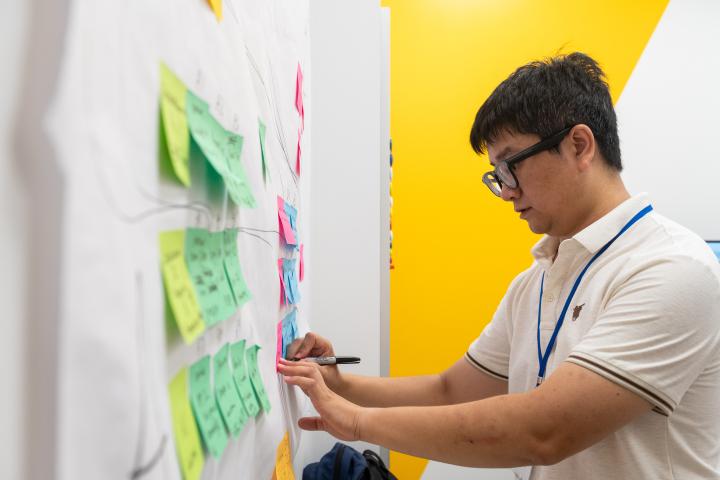 A Summer Studio 2025 participant writes on a sticky note that's pasted to a wall poster.