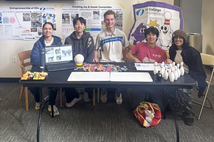 Students sit behind a table to showcase their BOW-ling project. 