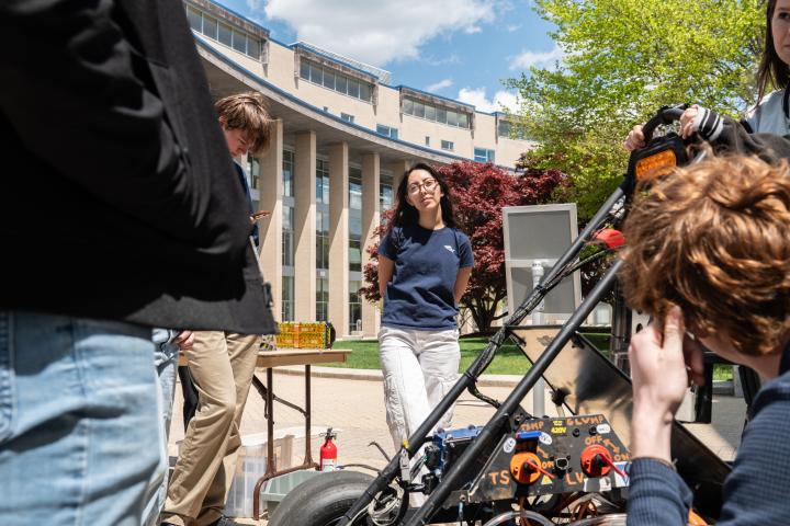 An Olin College of Engineering student is pictured outside on the Oval with the Miller Academic Building (MAC) in the background during Spring Expo 2026.