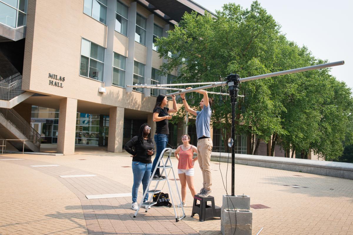 The Olin College SWARM-EX Team works together to experiment in the oval A group of students outside working on a sattelite