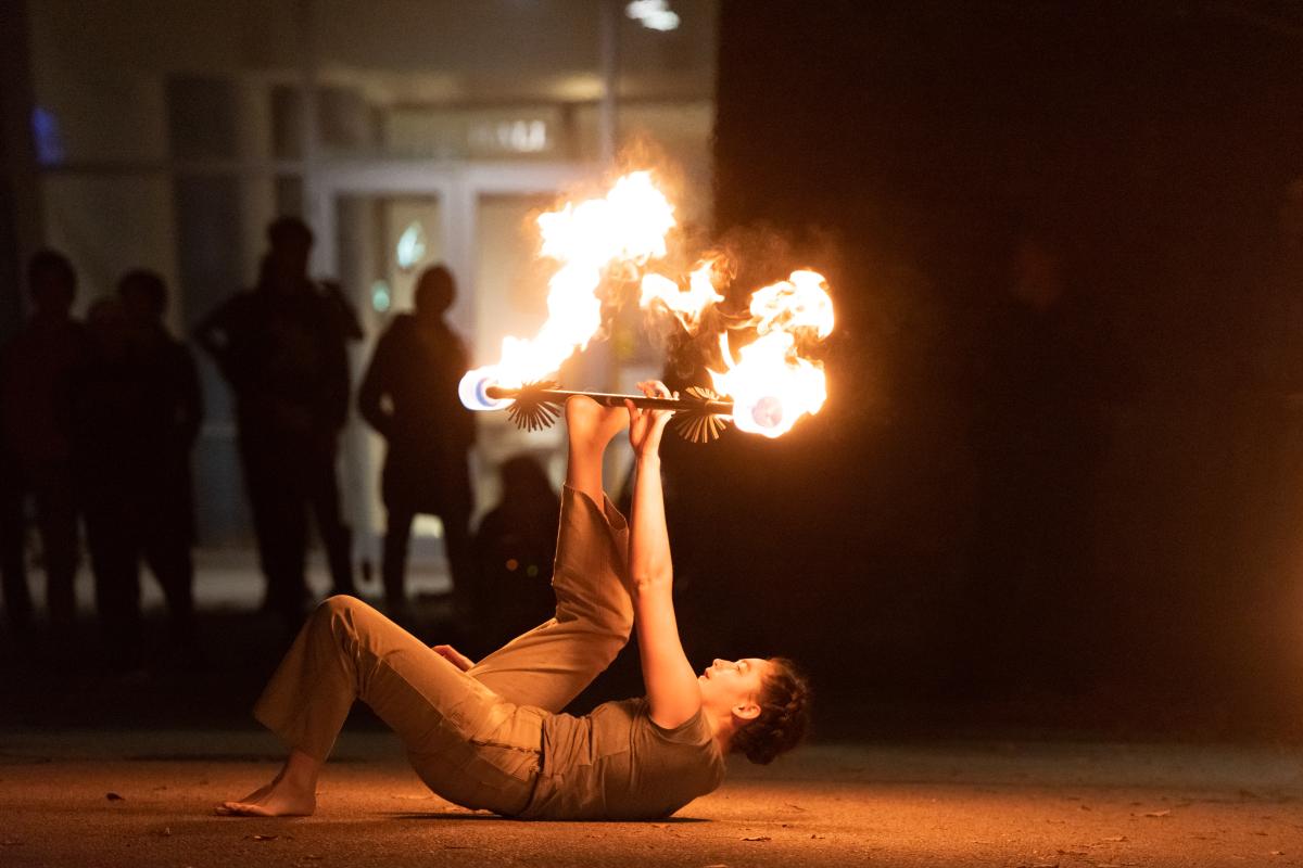 A member of the Olin College Fire Arts Club spins fire poi A photo of a person spinning fire poi