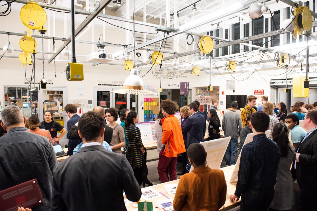 A group of people inside a large warehouse style building with yellow circles hanging from the ceiling