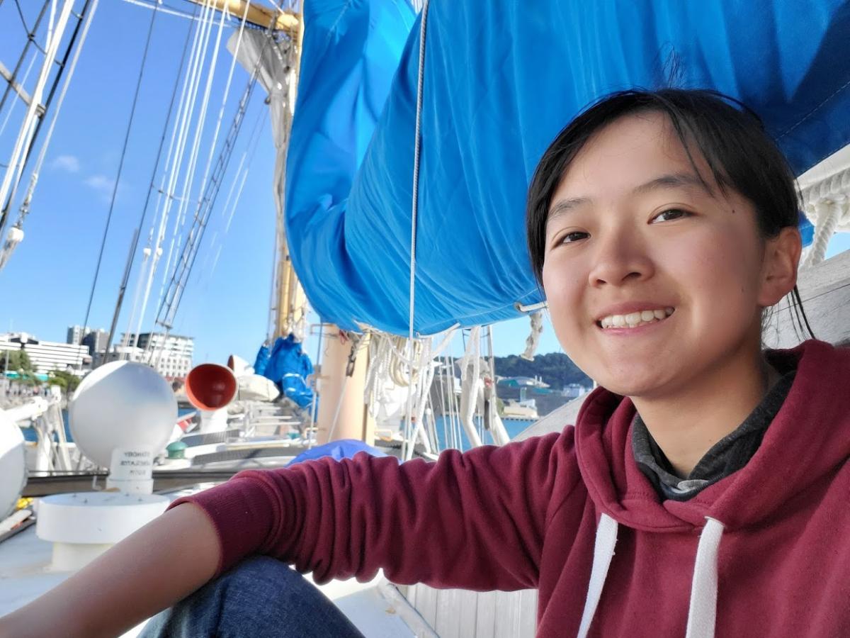 Amy Phung '21 sits on a boat with a blue sail in the background during a SEA Semester in Spring 2020.