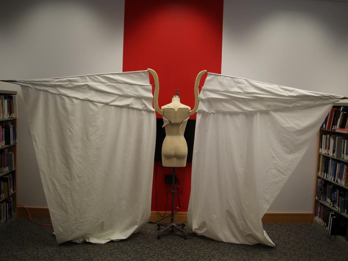 A dress form in the center of two sheets on its left and right, mimicking wings outstretched.
